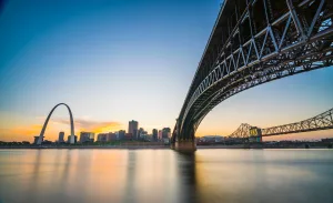 A bridge with a river with the St. Louis arch in the background